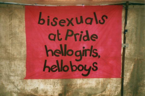 A banner on a tent wall reads "bisexuals at Pride / hello girls, / hello boys"