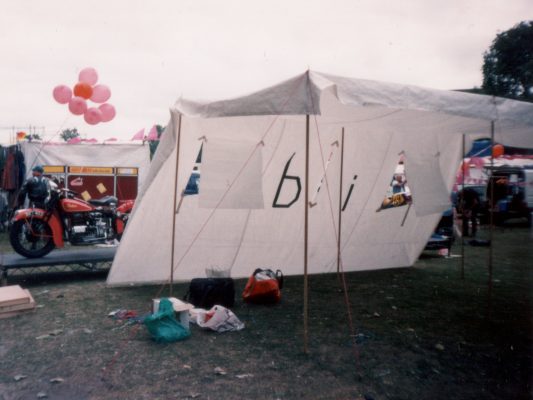 A large sheet of white material forming the back and roof of a stall. Poles support the roof, and two windows have been cut in the rear. The word 'bi' is on the back, made from some black tape